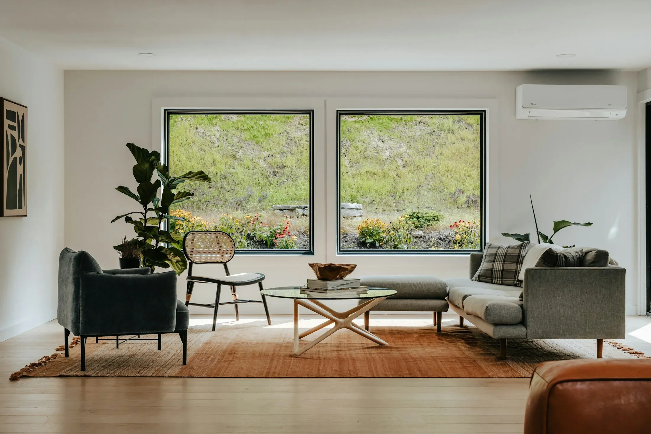 A bright living room with large windows, a sofa, chairs, and plants