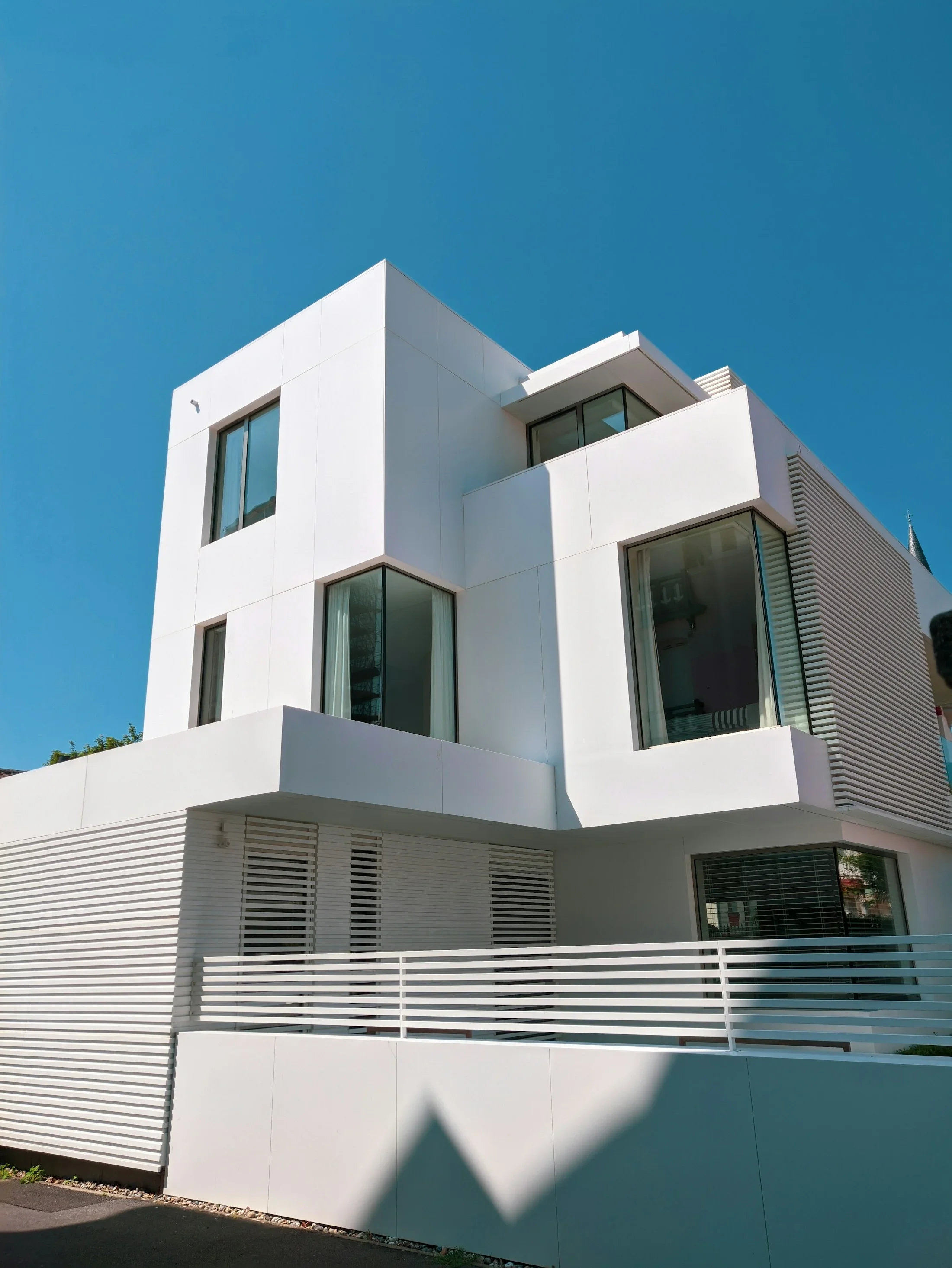 A contemporary white home with broad windows and angular exterior walls